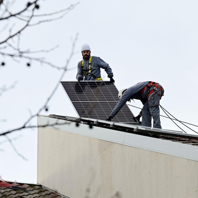 Des travailleurs sur un toit instalent un panneau solaire. 