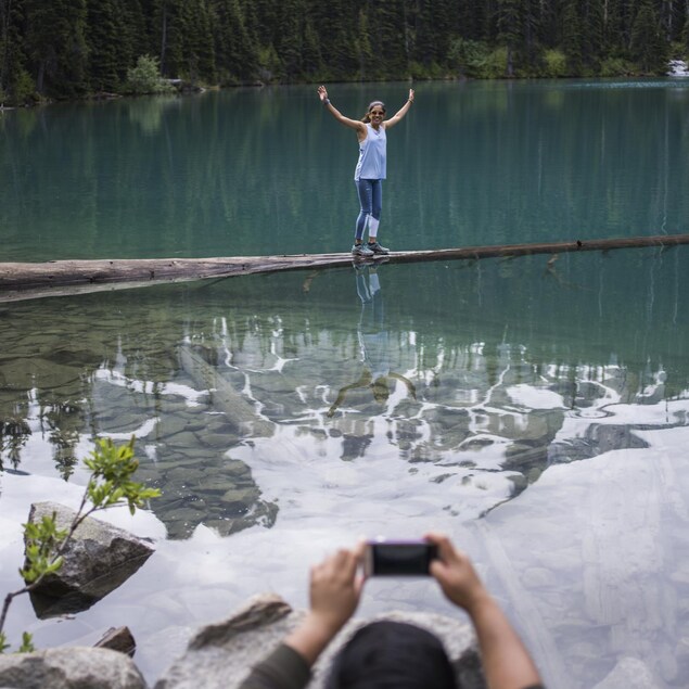 Une jeune femme se fait prendre en photo sur un tronc à demi-submergé aux abords d'un lac du parc britanno-colombien de Joffre Lakes.