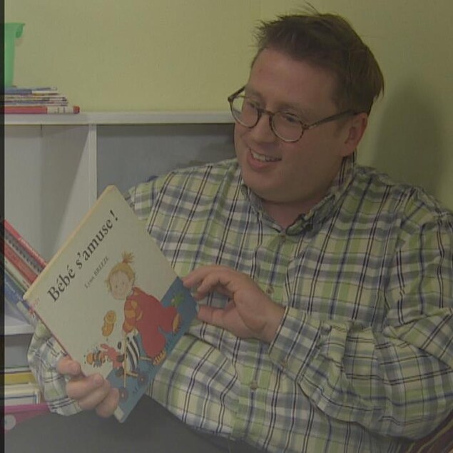 Au premier plan, couverture du recueil de poésie de Laurent Poliquin. En arrière plan, Laurent Poliquin lit un livre aux enfants de sa garderie en milieu familial. Au premier plan, couverture du recueil de poésie de Laurent Poliquin. En arrière plan, Laurent Poliquin lit un livre aux enfants de sa garderie en milieu familial.