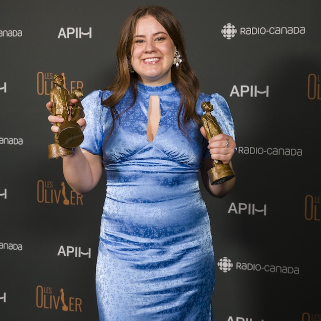 Une femme en robe bleue tient trois statuettes. 
