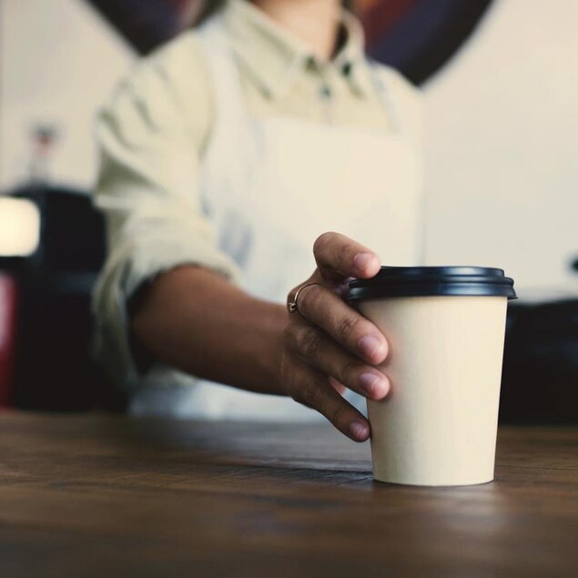 Une personne barista dépose un café sur le comptoir.