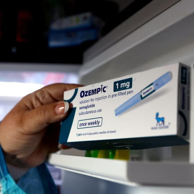 Closeup of a hand taking a box of Ozempic off a shelf.