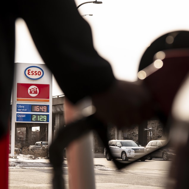 Silhouette d'une main qui tient une pompe à essence. Entre son tronc et son bras, on voit l'enseigne de la station-service et le prix de 1,64 $ le litre d'essence, et 2,12 $ le litre de diesel.