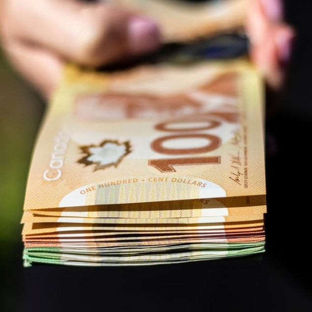 Une main qui tient une pile de billets de 100, 50 et 20 dollars canadiens.