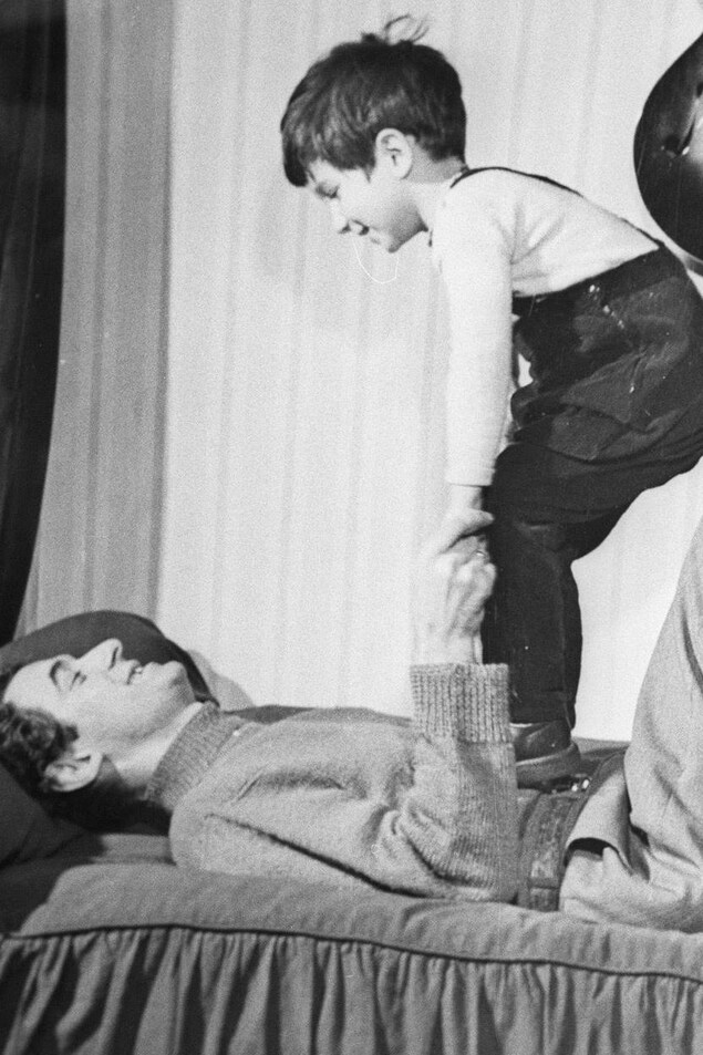 Félix Leclerc et son fils, Martin. Le chanteur dans la trentaine est couché et debout sur lui, son fils. Félix Leclerc et son fils, Martin. Le chanteur dans la trentaine est couché et debout sur lui, son fils.