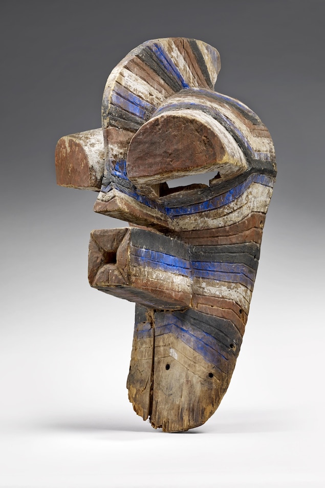Le crâne est divisé en deux sections par une arête qui prolonge le nez; les yeux sont des demie-cylindres pointés vers l'avant; le nez est triangulaire. Masque peint de couleurs rouge, bleu et blanc. Le crâne est divisé en deux sections par une arête qui prolonge le nez; les yeux sont des demie-cylindres pointés vers l'avant; le nez est triangulaire. Masque peint de couleurs rouge, bleu et blanc.