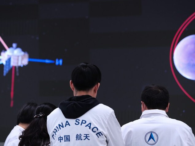 Des travailleurs de l'agence spatiale chinoise fixent un écran où l'on voit une image de sonde et la Lune.