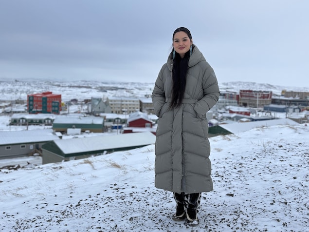Une femme vêtue d'un long manteau d'hiver se tient debout devant une vue enneigée d'Iqaluit, au Nunavut, en décembre 2024.