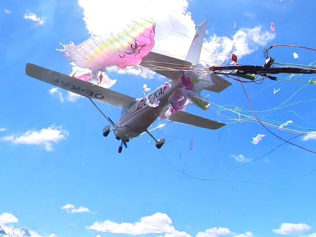 Un avion vole avec des bouts de parapente accrochés sur les ailes.