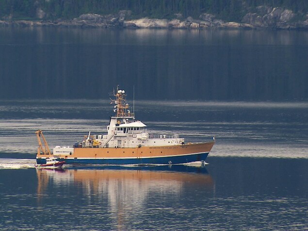On voit le navire de recherche Coriolis II et le bateau pneumatique Colvert glisser côte à côte sur les eaux calmes de la rivière Saguenay. On voit le navire de recherche Coriolis II et le bateau pneumatique Colvert glisser côte à côte sur les eaux calmes de la rivière Saguenay.