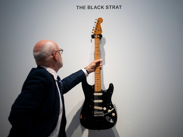 Un homme accroche la guitare noire sur un mur blanc.