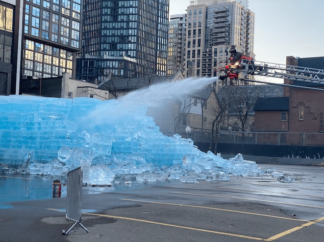 Un pompier sur une échelle arrose le bloc de glace dans un stationnement.