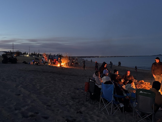 Des Nord-Côtiers sont réunis autour d'un feu de camp, sur une plage. 