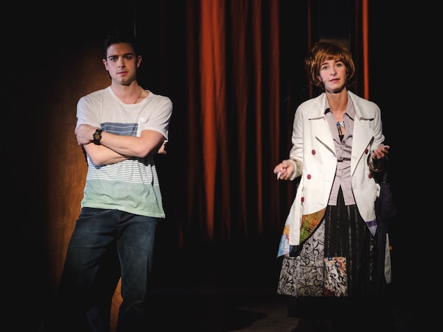 Une femme, sur une scène, tient une cigarette dans les mains aux côtés d'un homme