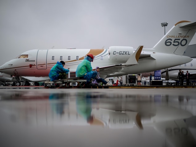 Des gens travaillent près d'un avion Bombardier 650 Challenger garé dans un aéroport.