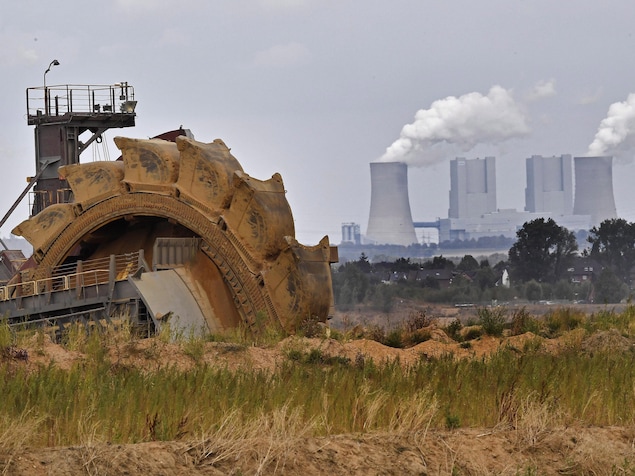 Une grosse machine creuse le sol. En arrière plan, la forêt et des cheminées d'usine. Une grosse machine creuse le sol. En arrière plan, la forêt et des cheminées d'usine.