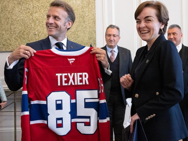 Emmanuel Macron tient un un chandail d'Alexandre Texier, debout aux côtés de Christine Fréchette.