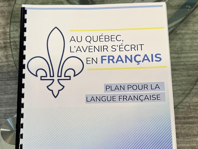 Sur une table, un document officiel du gouvernement du Québec où il est inscrit « Au Québec, l'avenir s'écrit en français : Plan pour la langue française ».