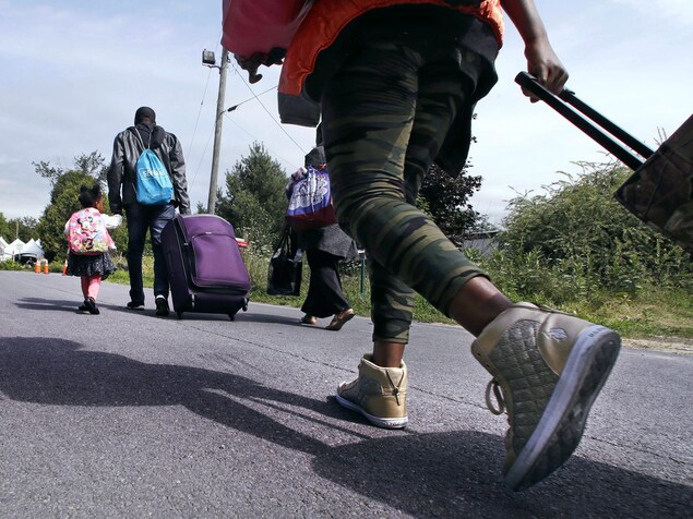 Des migrants haïtiens marchent sur une route en traînant leurs valises. Des migrants haïtiens marchent sur une route en traînant leurs valises.