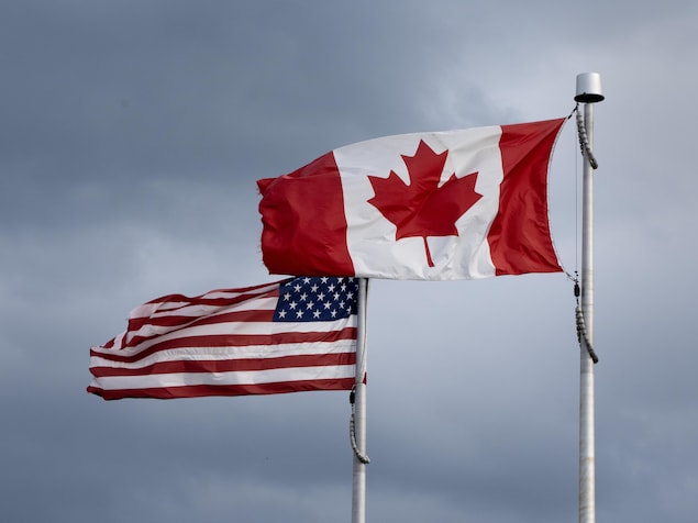 Les drapeaux du Canada et des États-Unis flottent devant un ciel nuageux au sommet de deux mâts.
