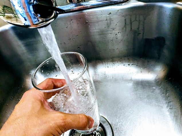 Une main tient un verre qui se remplit d'eau sous le robinet d'un évier.