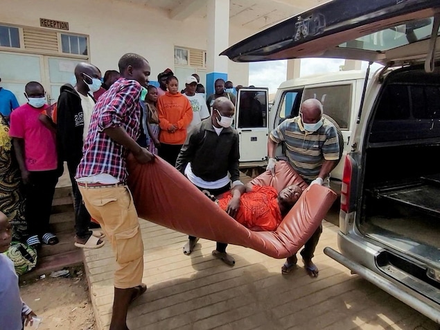 Des gens sortent un malade couché sur un matelas d'une camionnette.