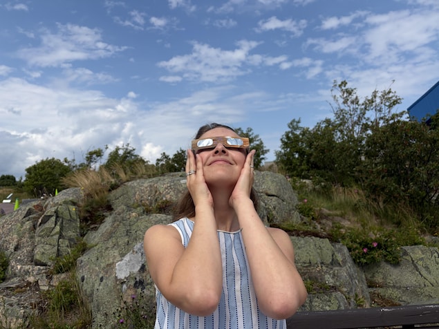 Une femme regarde le ciel avec des lunettes spéciales pour regarder le soleil.