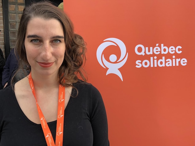 Une jeune femme pose devant une affiche de Québec Solidaire.