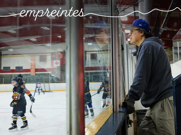 Doug Cheechoo regarde des hockeyeurs sur le bord d'une patinoire. 