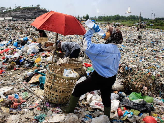 Une femme boit de l'eau en bouteille au milieu de milliers de déchets de plastique