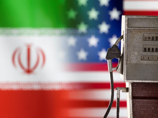 Une pompe d'essence avec en fond des drapeaux de l'Iran et des États-Unis.