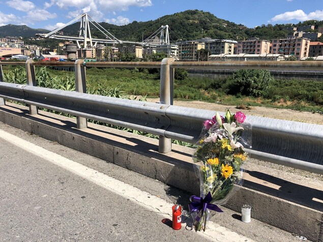 Un bouquet composé de différentes fleurs et des chandelles sont posées le long d'une autoroute. En arrière-plan, on peut voir un pont dont une partie est manquante. Un bouquet composé de différentes fleurs et des chandelles sont posées le long d'une autoroute. En arrière-plan, on peut voir un pont dont une partie est manquante.