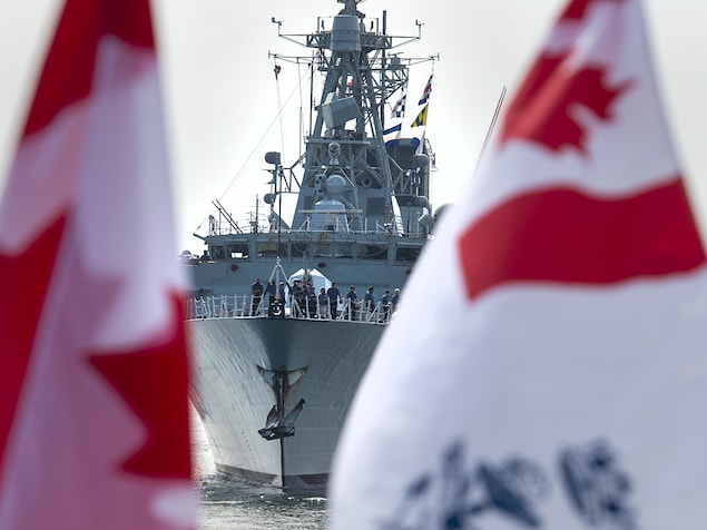 Une frégate photographiée derrière des drapeaux canadiens.