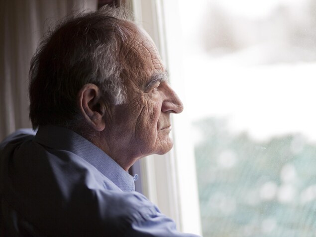 Un homme âgé regarde par la fenêtre. Un homme âgé regarde par la fenêtre.