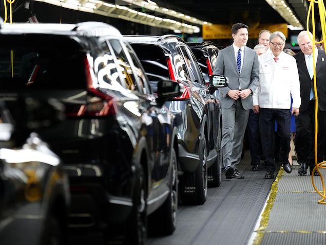 Le premier ministre Justin Trudeau, le dirigeant de Honda, Toshihiro Mibe, et le premier ministre de l'Ontario, Doug Ford, marchent le long d'une chaîne de montage de voitures.