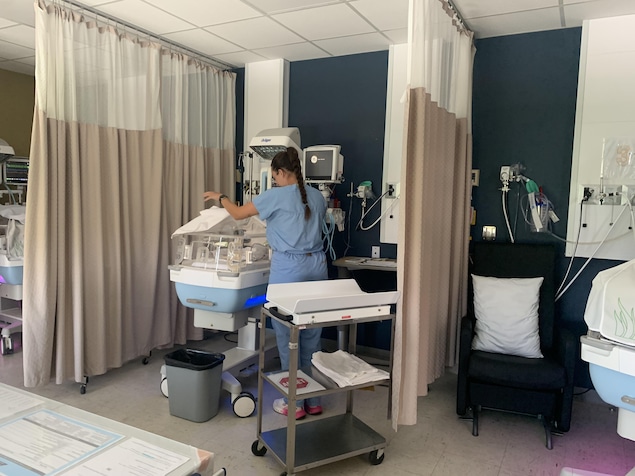 Une infirmière, de dos, devant un incubateur.