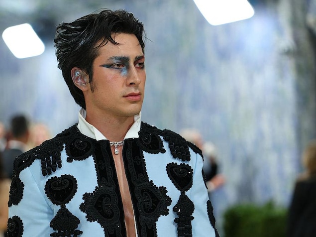 L’acteur canadien Hudson Williams, avec un maquillage bleu autour des yeux et une veste bleu poudre ornée de motifs floraux noirs et d’un col blanc.