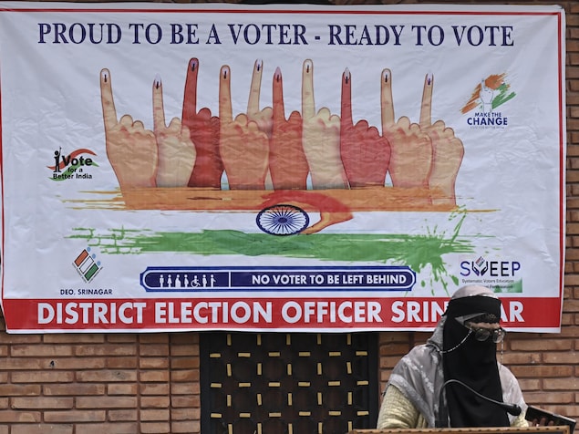 Une femme voilée devant une affiche incitant les électeurs à voter.