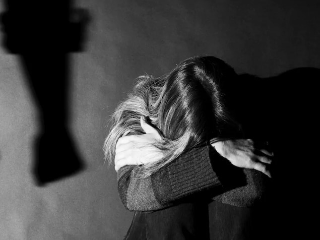 Une femme assise, se cachant les yeux pour ne pas voir son partenaire violent.