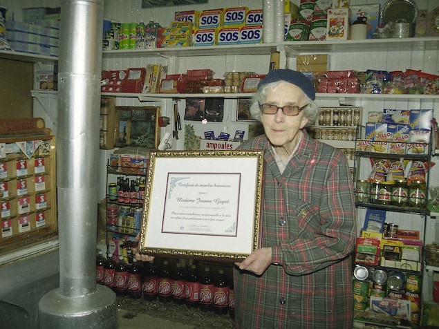 Une femme devant des étalages d'épicerie, elle tient un certificat entre ses mains.