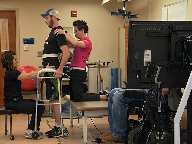 Un homme paraplégique se tient debout avec l'aide de deux thérapeutes. Un homme paraplégique se tient debout avec l'aide de deux thérapeutes.