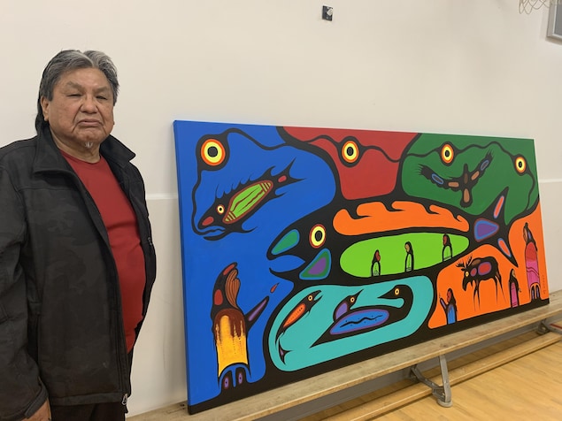 Frank Polson, qui fixe la caméra, pose à quelques pas de sa fresque.