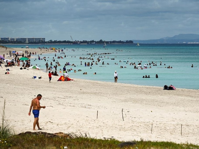 Des touristes profitent de leurs vacances sur une plage de sable blanc devant une mer bleu claire. 