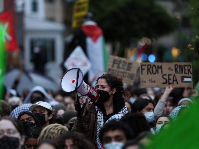Une femme utilise un porte-voix pendant que des étudiants et d'autres manifestent dans un campement de protestation.