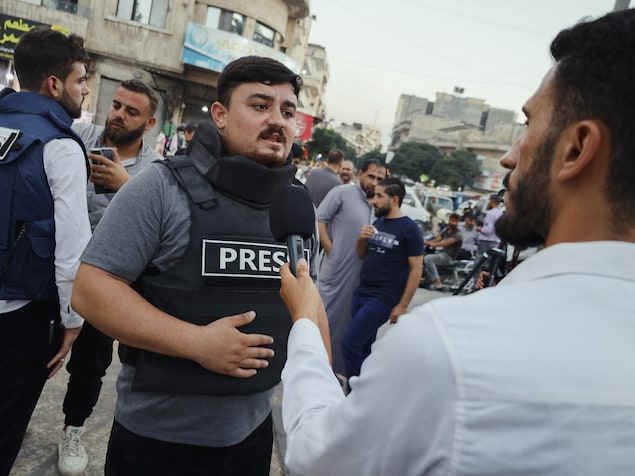 Un journaliste portant un gilet de presse s'adresse à un reporter lors d'un rassemblement de solidarité à Idlib, en Syrie, le 11 août 2025. 