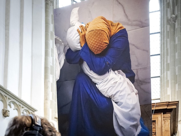 Une photo montrant une femme prenant dans ses bras un corps enveloppé d'un linceul. 