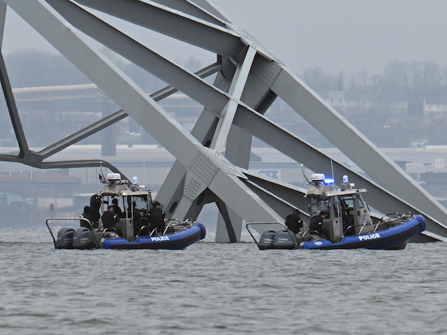 Deux bateaux de la police flottent à côté d'un immense morceau de la structure du pont en acier qui s'est effondré dans l'eau.