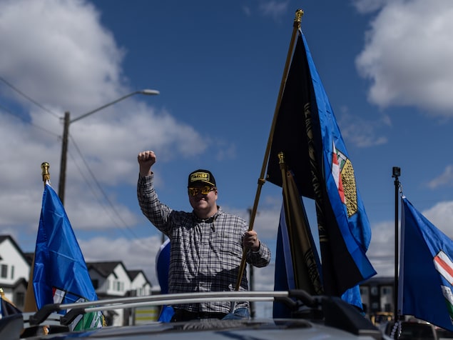 Une personne agite un drapeau sur le toit d'un véhicule.