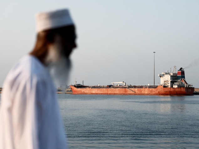 Une personne marche devant un pétrolier ancré dans un port.