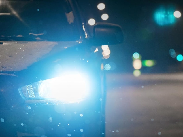 Gros plan sur un phare de voiture allumé par une nuit de neige.